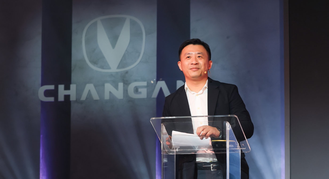Mr. Yin in a suit stands at a clear podium, confidently smiling, with the Changan logo and name illuminated in the background.